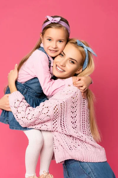 Feliz hija sonriendo mientras abrazando madre aislado en rosa - foto de stock