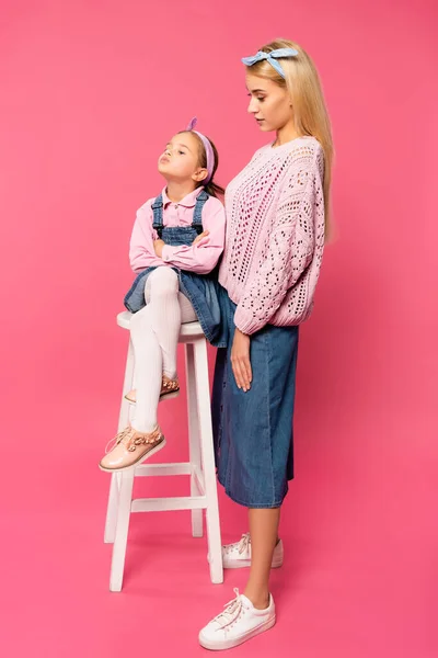 Longitud completa de la madre mirando ofendido niño sentado en la silla en rosa - foto de stock