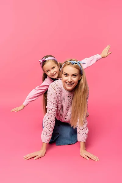 Мати посміхається біля дочки з простягнутими руками на рожевому — стокове фото