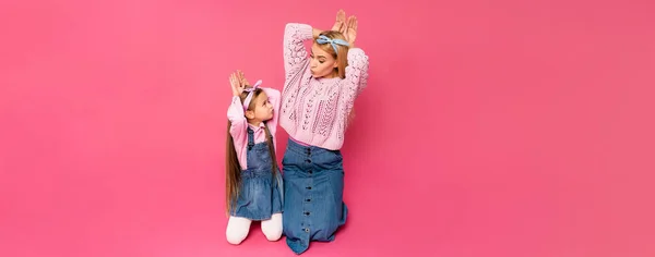 Mutter und Tochter basteln Hasenohren mit den Händen und schauen sich auf rosa Transparenten an — Stockfoto