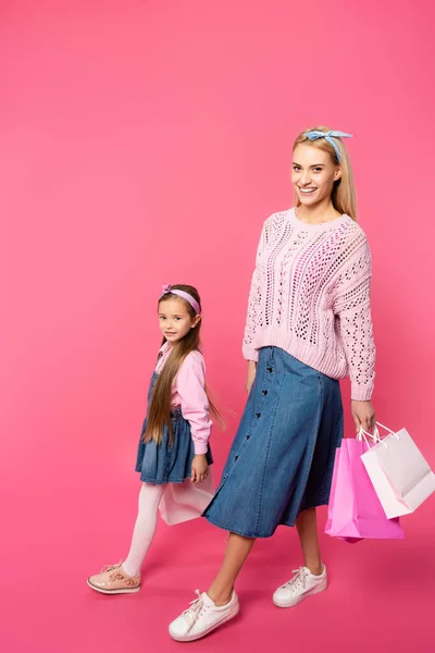 Happy mother and daughter walking with shopping bags on pink — Stock Photo