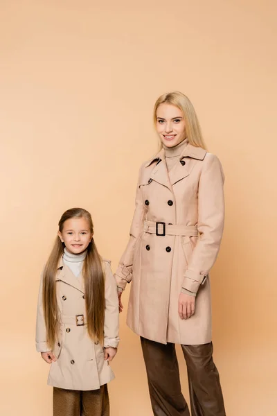 Mother and daughter in trench coats smiling while standing isolated on beige — Stock Photo