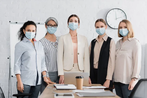 Mulheres de negócios multiculturais em máscaras médicas perto do local de trabalho na sala de reuniões — Fotografia de Stock