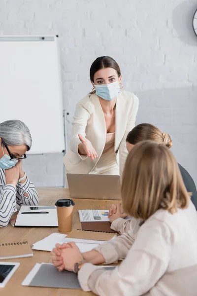 Líder del equipo en máscara médica apuntando con la mano a la mujer de negocios durante el seminario - foto de stock