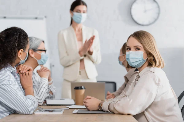 Junge Geschäftsfrau blickt in Kamera in der Nähe von interrassischen Mitarbeitern auf verschwommenem Hintergrund — Stockfoto