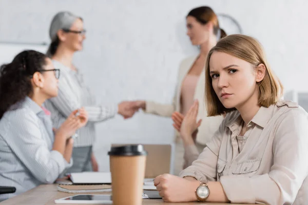 Serious businesswoman looking at camera near interracial coworkers on blurred background — Stock Photo