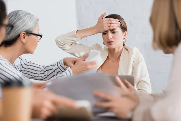 Worried businesswoman looking at smartphone near interracial colleagues on blurred foreground — Stock Photo