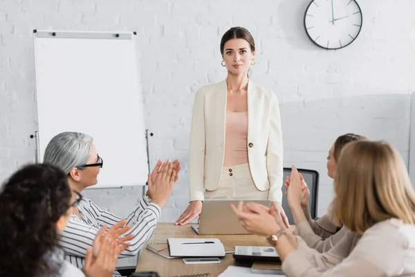 Selbstbewusster Teamleiter blickt in die Kamera, während multikulturelles Publikum auf verschwommenem Vordergrund applaudiert — Stockfoto