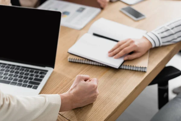 Vue recadrée de femme d'affaires avec poing serré près de gadgets et collègue au bureau — Photo de stock