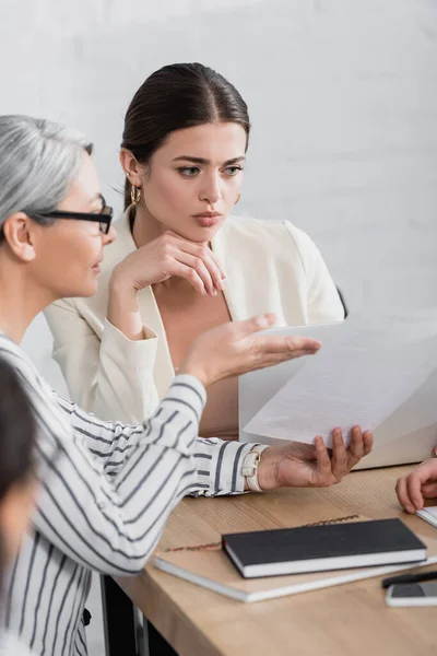 Asian businesswoman pointing with hand at document near colleague in office — Stock Photo