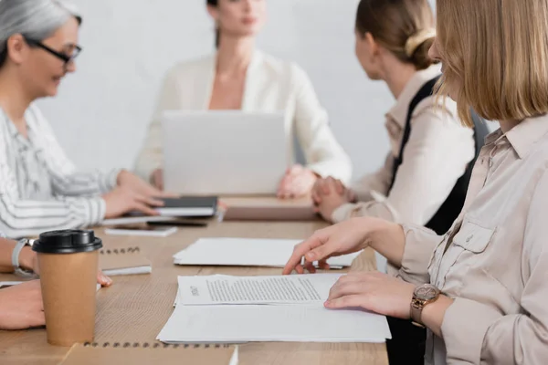 Empresária perto do contrato na mesa durante a reunião e colegas de trabalho em segundo plano — Fotografia de Stock