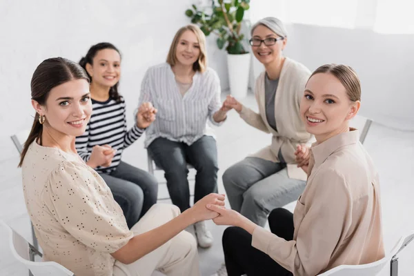 Heureuses femmes multiculturelles tenant la main et regardant la caméra — Photo de stock