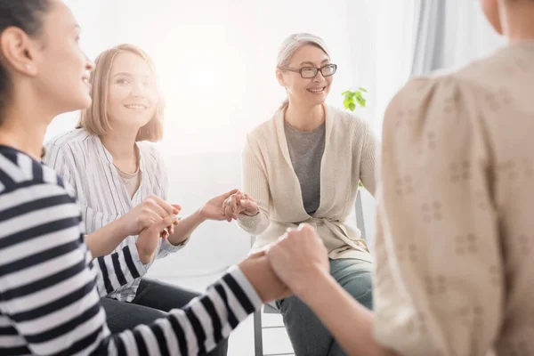 Mujeres multiculturales felices cogidas de la mano y sonriendo durante el seminario - foto de stock