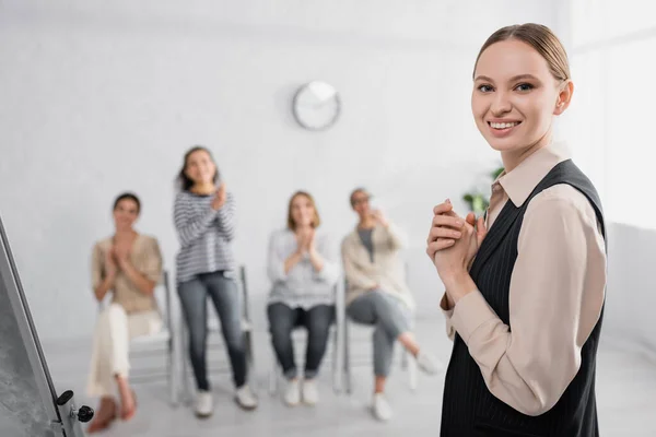 Cheerful businesswoman smiling near interracial coworkers on blurred background — Stock Photo