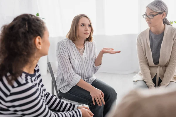 Empresaria señalando con la mano mientras está sentada cerca de compañeros de trabajo multiculturales - foto de stock