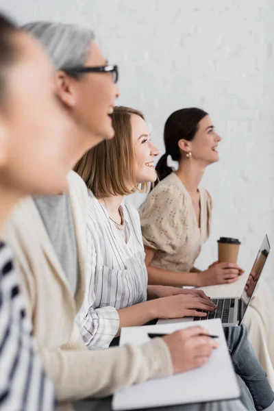 Fröhliche Frau lächelt in der Nähe einer multikulturellen Frauengruppe während eines Seminars über verschwommenen Vordergrund und Hintergrund — Stockfoto