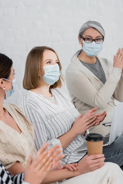 Multiethnic businesswomen in medical masks applauding during seminar — Stock Photo