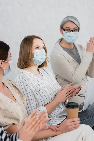 Empresarias multiétnicas con máscaras médicas aplaudiendo durante el seminario - foto de stock