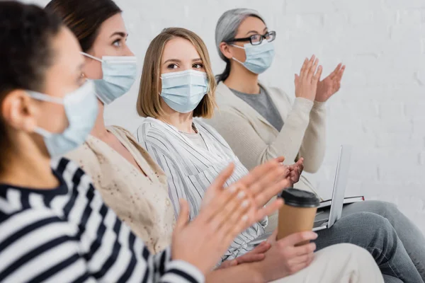 Multiethnic businesswomen in medical masks applauding during seminar in meeting room — Stock Photo