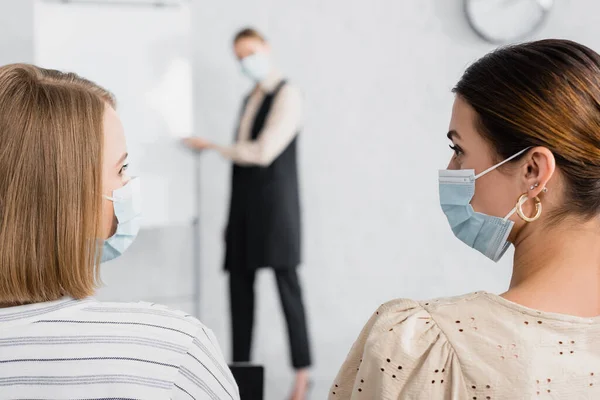 Jóvenes empresarias con máscaras médicas mirándose durante el seminario - foto de stock