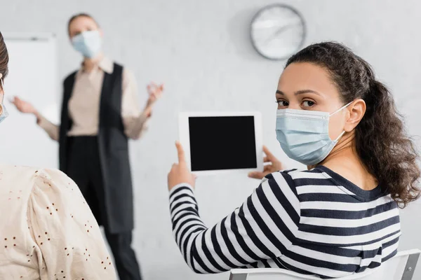 Femme afro-américaine en masque médical tenant tablette numérique avec écran vide près du haut-parleur — Photo de stock