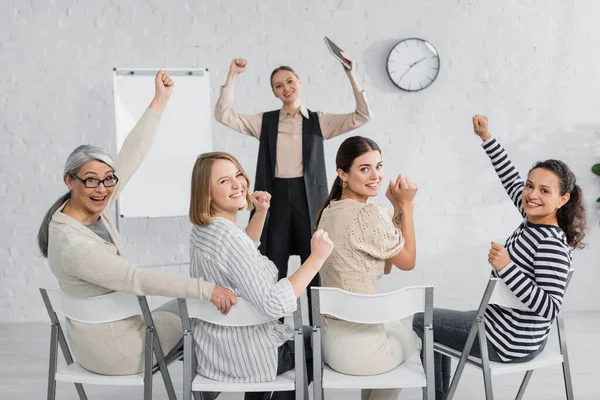 Excited interracial businesswomen and speaker with raised hands during lecture — Stock Photo