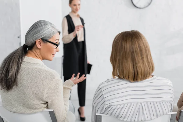 Asian businesswoman gesturing while talking with coworker during seminar — Stock Photo