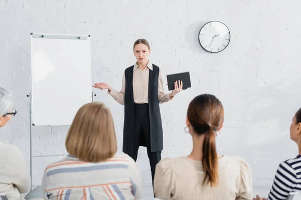 Young speaker holding notebook and looking at audience of women during seminar — Stock Photo