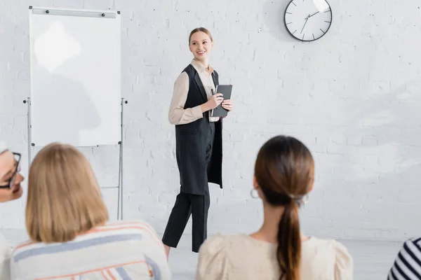 Junge Rednerin hält Notizbuch in der Hand und lächelt in der Nähe von Frauen während des Seminars — Stockfoto