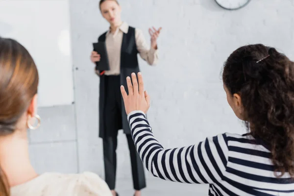 African american woman with raised hand near coworker and speaker of blurred background — Stock Photo