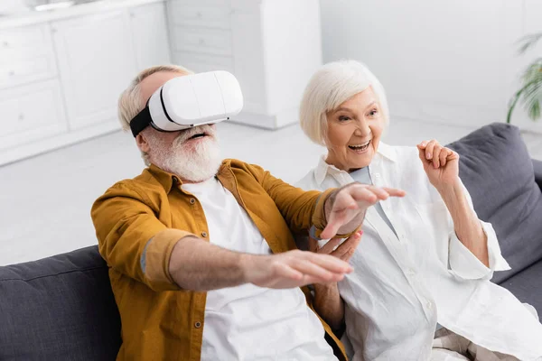 Senior man using vr headset near smiling wife in living room — Stock Photo
