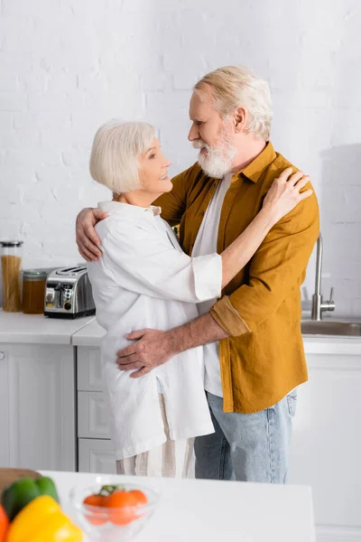 Couple de personnes âgées étreignant et souriant à l'autre près de légumes frais sur le premier plan flou — Photo de stock
