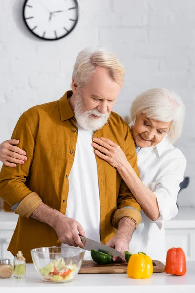 Senior schneidet Paprika neben lächelnder Frau in Küche — Stockfoto