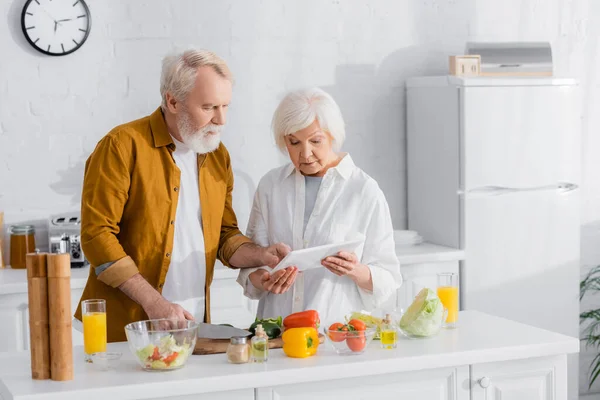 Seniorenpaar nutzt digitales Tablet beim Kochen in Küche — Stockfoto