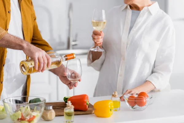 Vista cortada do homem derramando vinho perto da esposa e legumes em primeiro plano desfocado — Fotografia de Stock