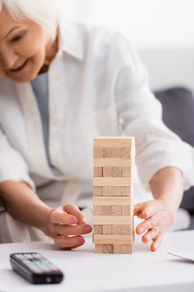 Blocks wood tower game near senior woman and remote controller on blurred foreground — Stock Photo