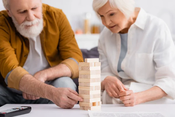Blocks wood tower game near elderly couple on blurred background in living room — Stock Photo