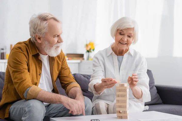 Elderly couple playing blocks wood tower game in living room — Stock Photo