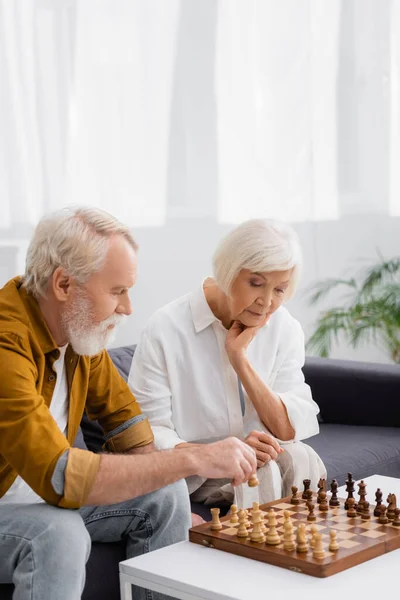 Pareja mayor jugando al ajedrez en el sofá en la sala de estar - foto de stock