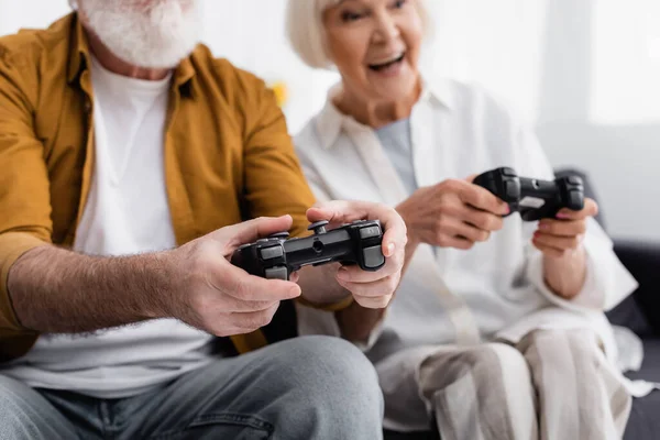 KYIV, UKRAINE - DECEMBER 17, 2020: Gamepads in hands of elderly couple playing video game on blurred background — Stock Photo