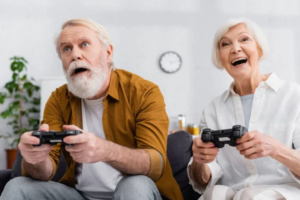 KYIV, UKRAINE - DECEMBER 17, 2020: Excited elderly couple playing video game together at home — Stock Photo