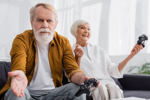 KYIV, UKRAINE - DECEMBER 17, 2020: Confused man holding joystick near excited wife on blurred background — Stock Photo