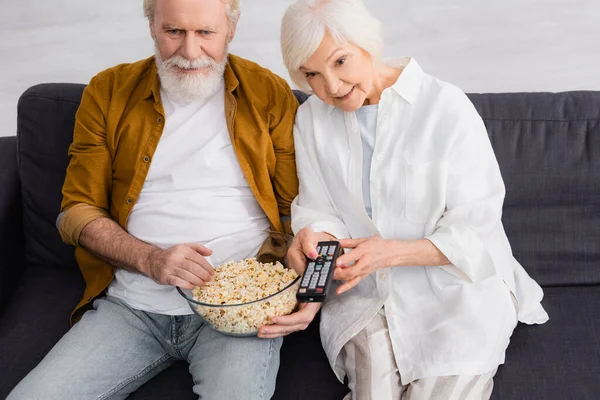 Couples âgés regardant la télévision et tenant du pop-corn dans le salon — Photo de stock