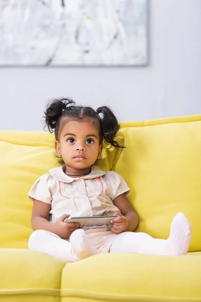 Toddler african american girl holding smartphone while sitting on sofa — Stock Photo