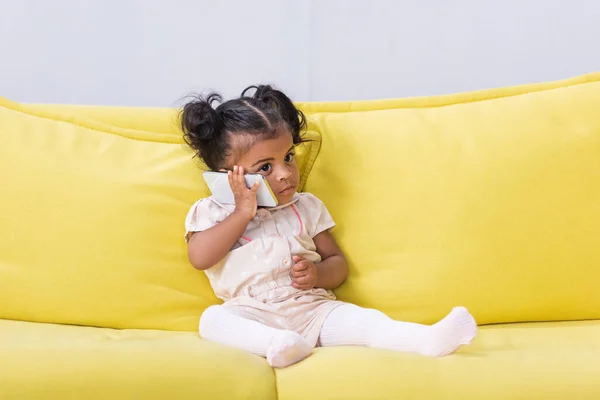 Afrikanisch-amerikanische Kleinkind Mädchen spricht auf Smartphone, während es auf dem Sofa sitzt — Stockfoto