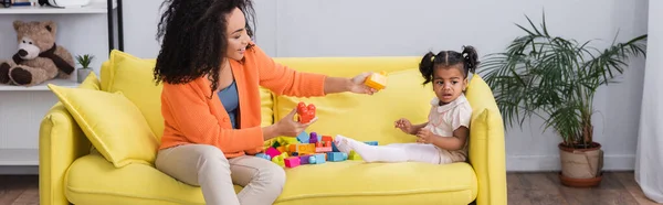 Happy african american mother playing building blocks with toddler kid on sofa, banner — Stock Photo