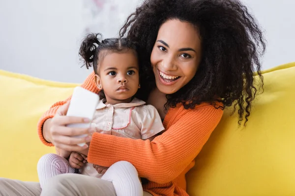 Glückliche afrikanisch-amerikanische Mutter hält Smartphone und macht Selfie mit Kleinkind-Tochter — Stockfoto