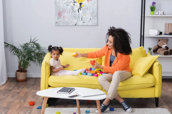 Glückliche afrikanisch-amerikanische Mutter spielt Bauklötze mit Kleinkind auf Sofa — Stockfoto