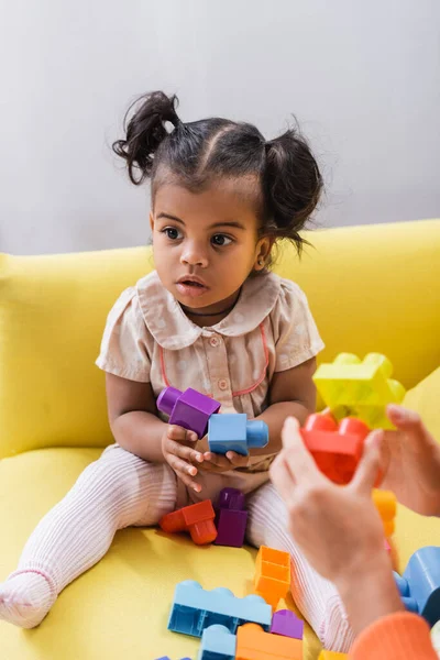 Afrikanisch-amerikanisches Kleinkind sitzt auf Sofa und spielt Bauklötze mit Mutter auf verschwommenem Vordergrund — Stockfoto