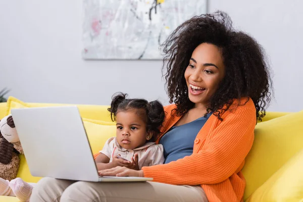 Felice freelance africano americano utilizzando laptop vicino alla figlia del bambino in soggiorno — Foto stock